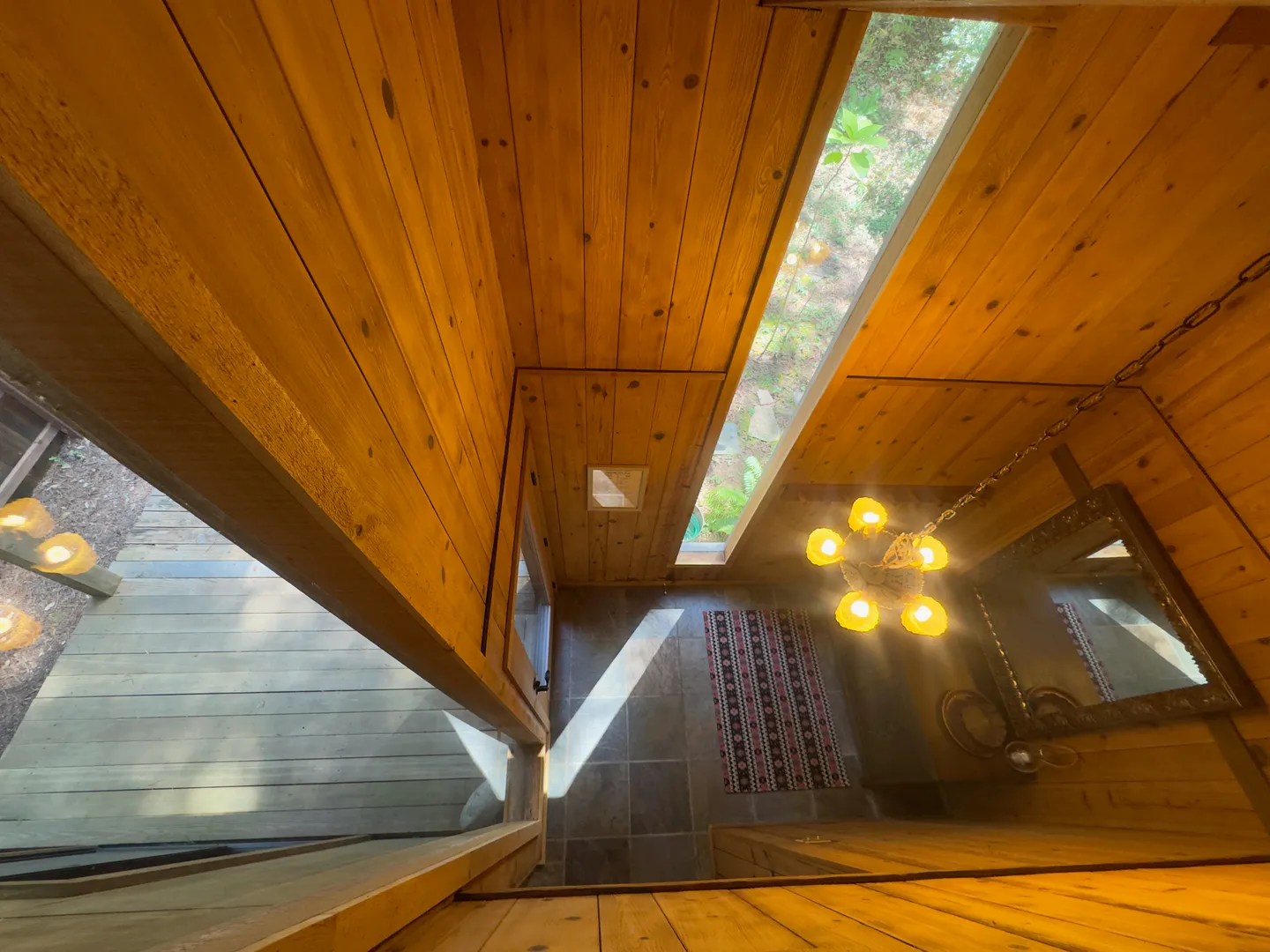 High-angle view looking down into a wood-paneled entryway with tile floors, a patterned rug, and a warm hanging chandelier.