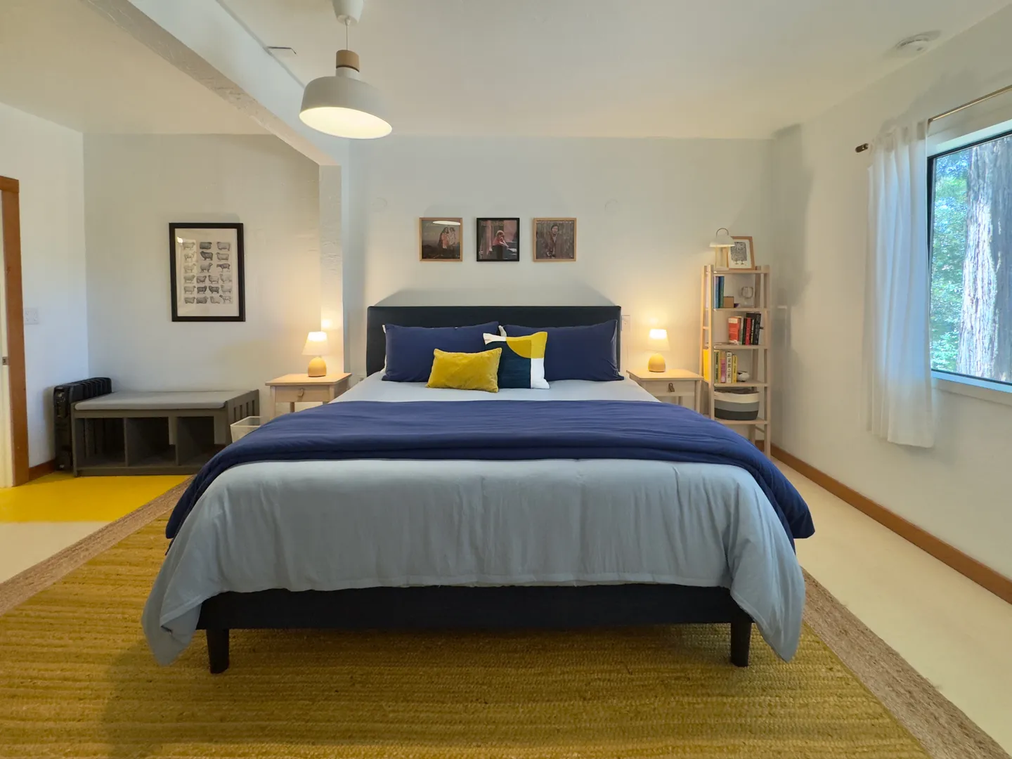Bedroom with a dark headboard, blue bedding, nightstands with small lamps, and a yellow area rug.