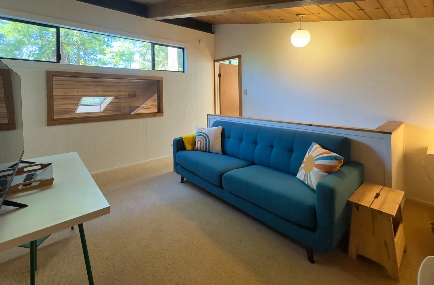 Upstairs loft sitting area with a blue tufted sofa, wooden ceiling, and clerestory windows.