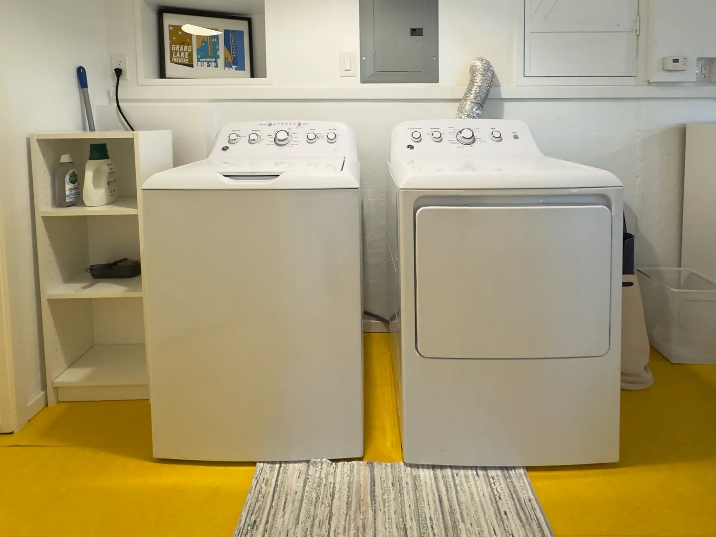 A white top-loading washing machine and matching dryer set against a white wall with yellow flooring.