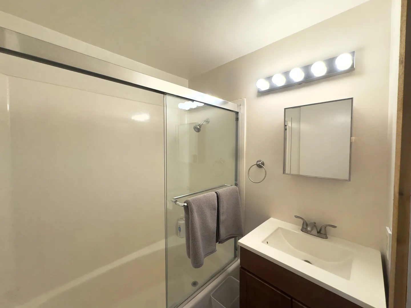 Bathroom showing a tub and shower combination with sliding glass doors beside a vanity sink and mirrored medicine cabinet.