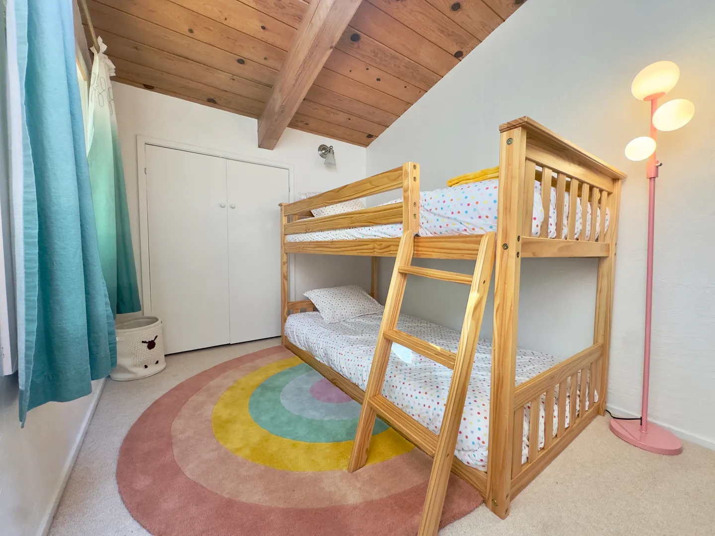 Bedroom featuring a wooden bunk bed, rainbow circular rug, and vaulted wood-plank ceiling with exposed beams.