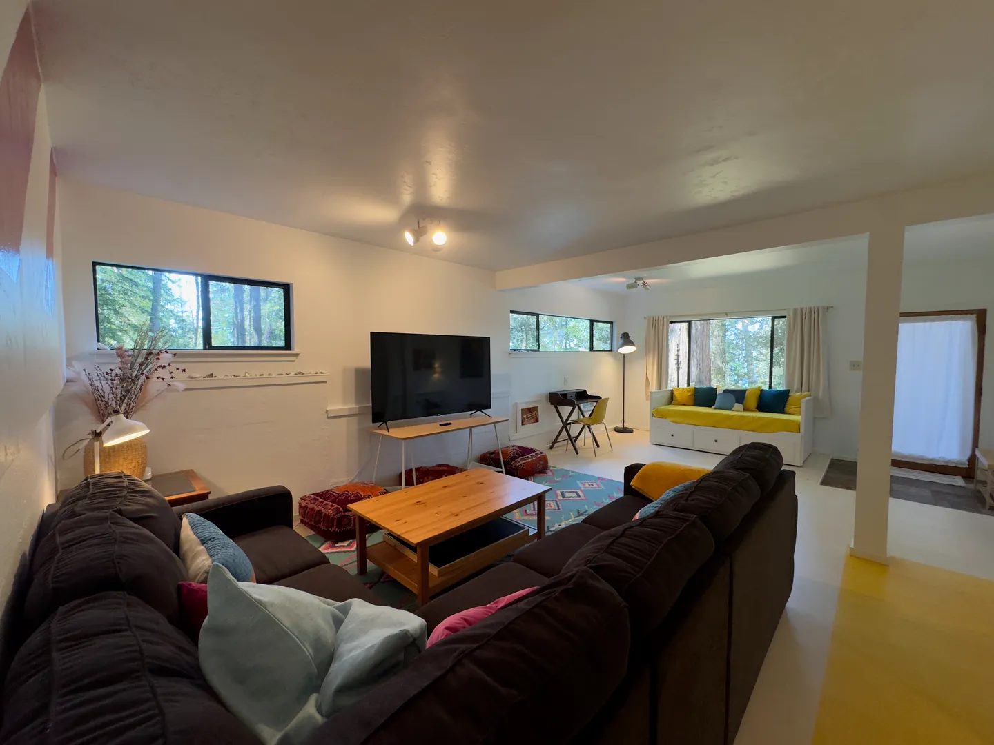 Living room with a dark sectional sofa, coffee table, television, and windows overlooking trees.