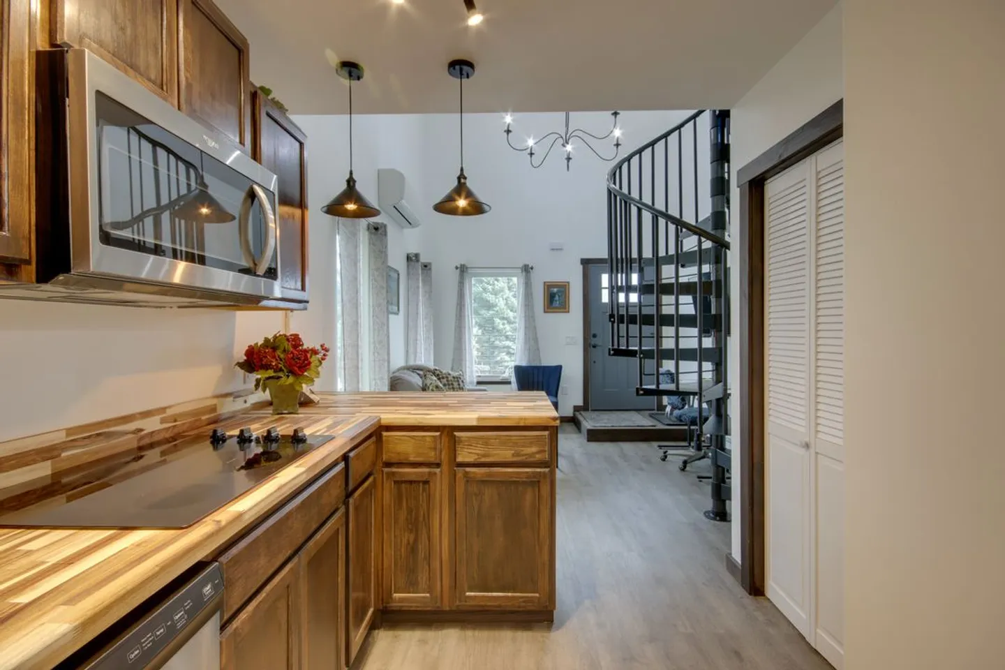 Kitchen counter with butcher block countertop leading toward a living area with a black spiral staircase.