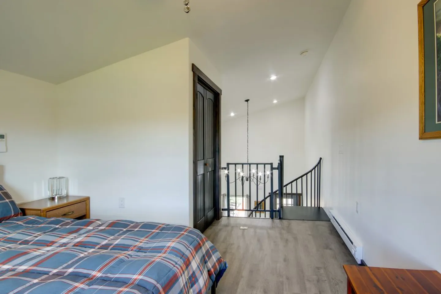 Upstairs bedroom area overlooking a stairwell with black metal railings and a hanging chandelier.
