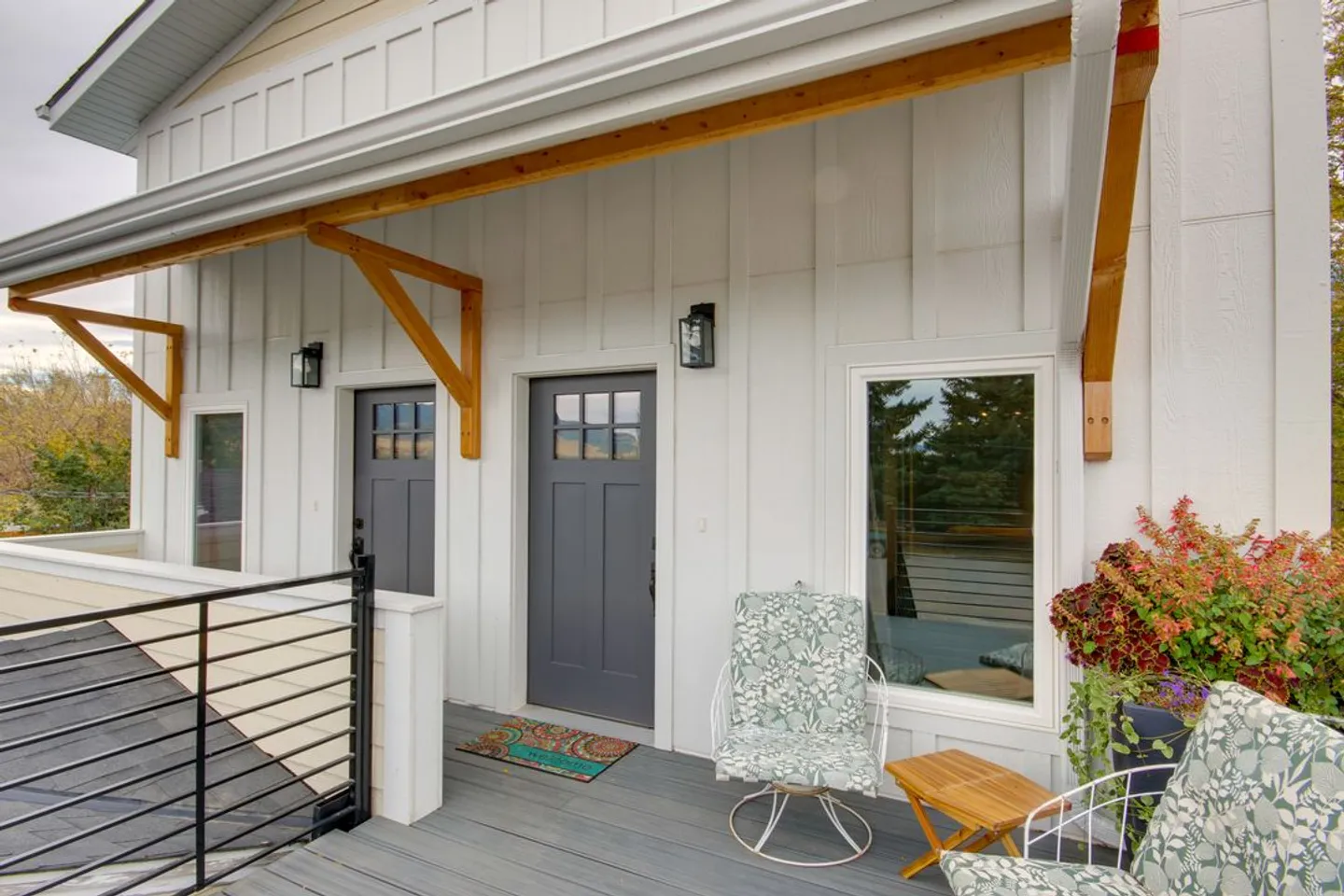 Exterior covered porch with white board-and-batten siding, dark gray doors, and patio chairs.