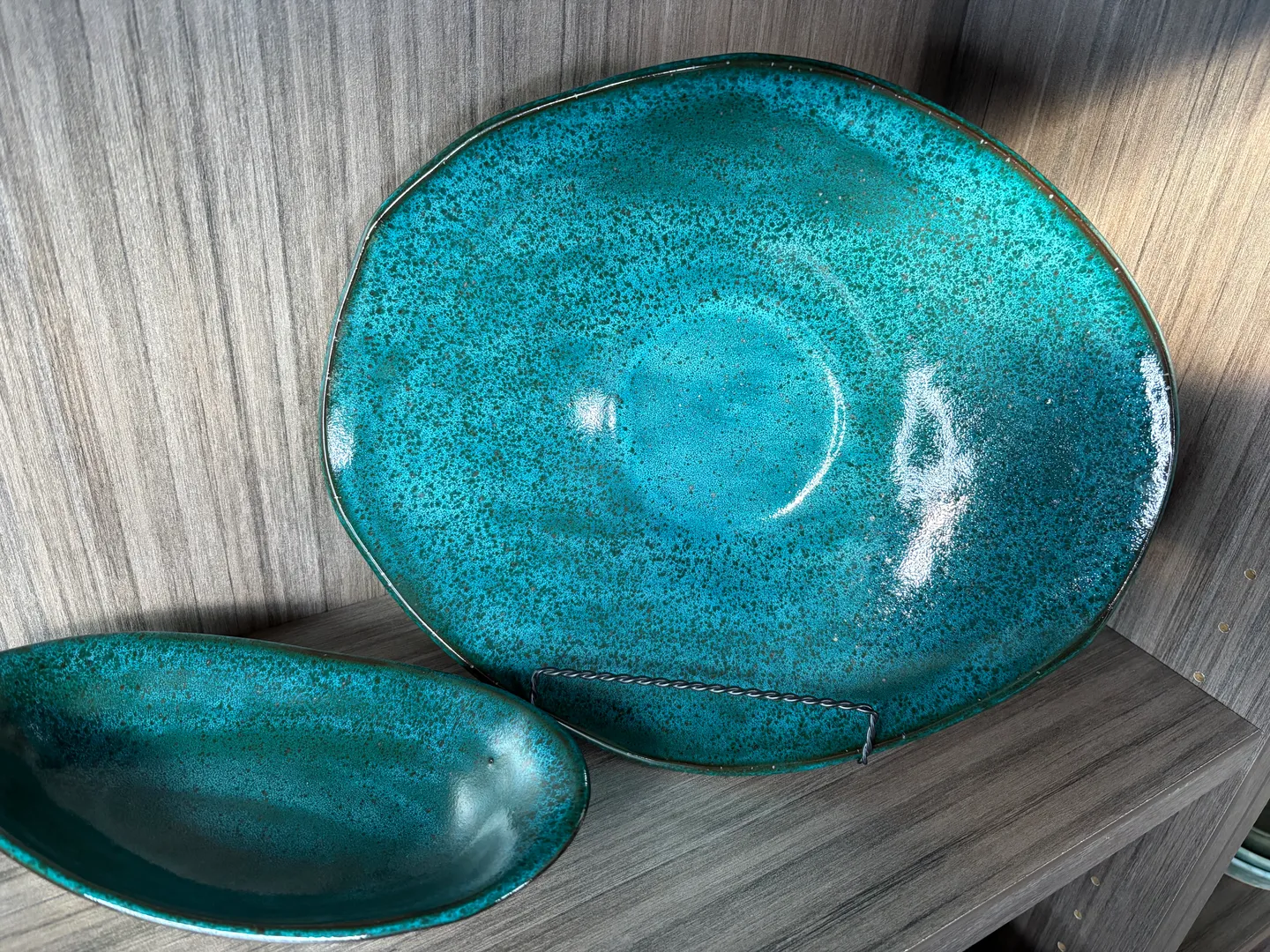 Decorative turquoise ceramic plate on a display stand next to a matching bowl on a wooden shelf.