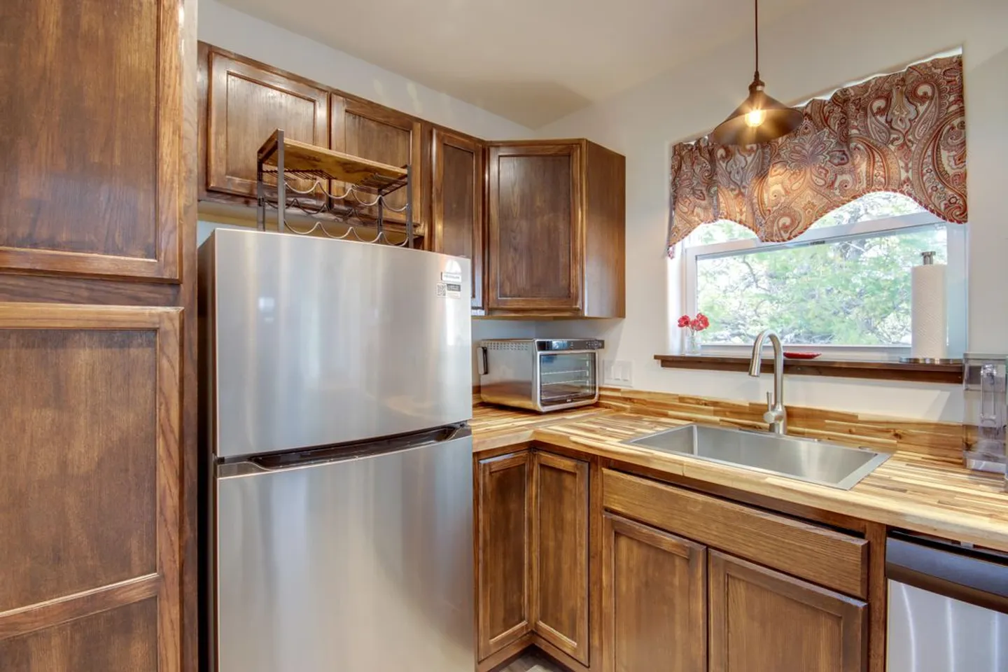 Kitchen corner with stainless steel refrigerator, sink under a window, wood cabinets, and butcher block countertops.