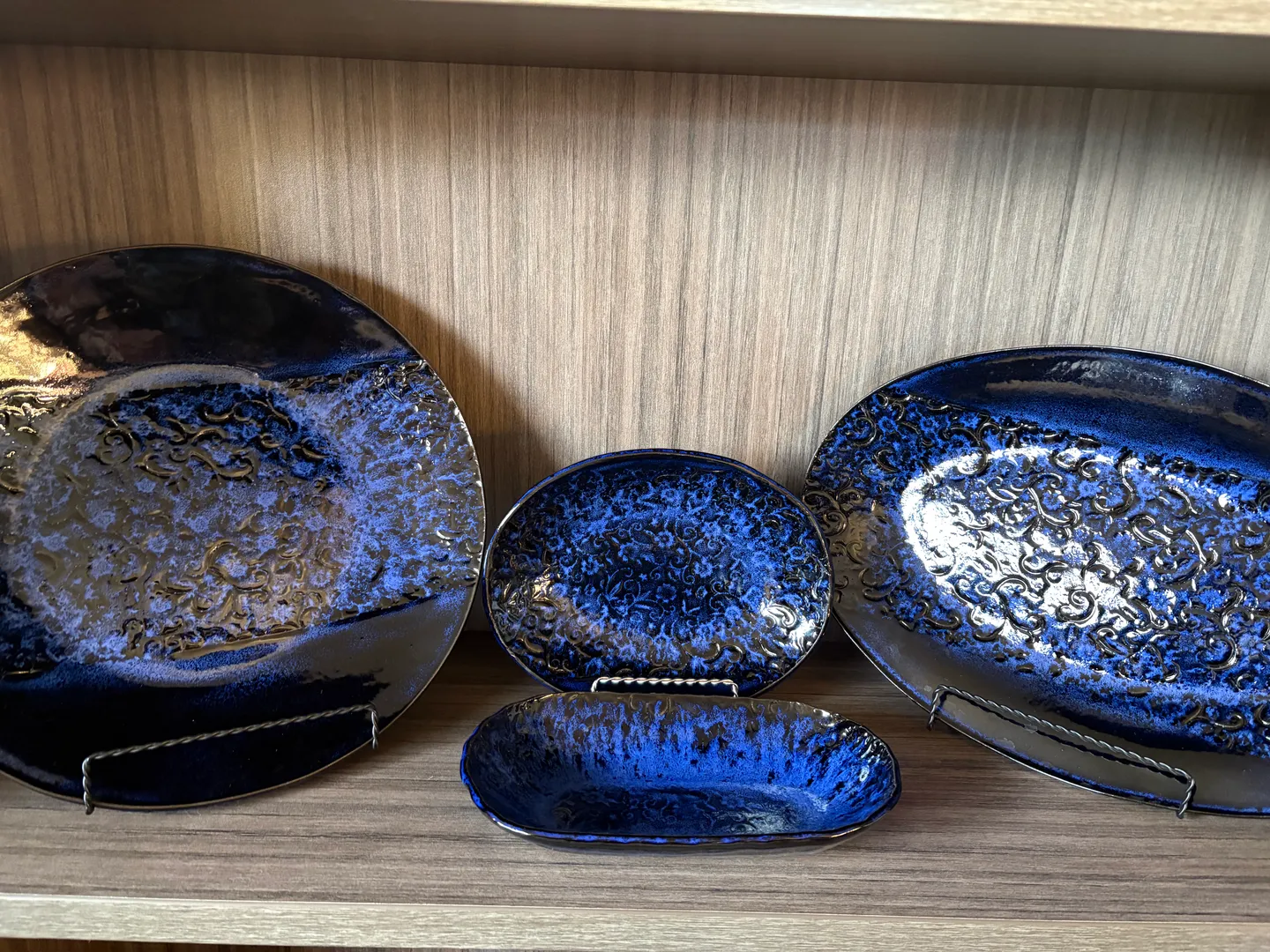 A close-up of decorative blue glazed ceramic plates and bowls displayed on a wooden shelf.