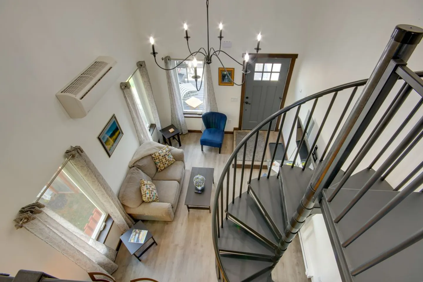 High-angle view of a living area featuring a spiral staircase, a sofa, coffee table, and front entry door under a chandelier.