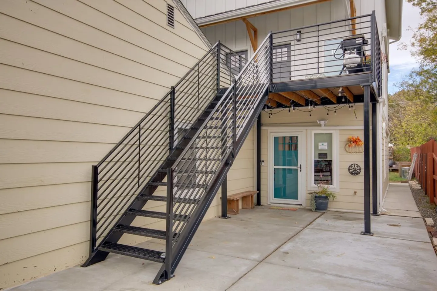 Exterior black metal staircase leading up to an elevated deck and entrance beside a concrete patio.