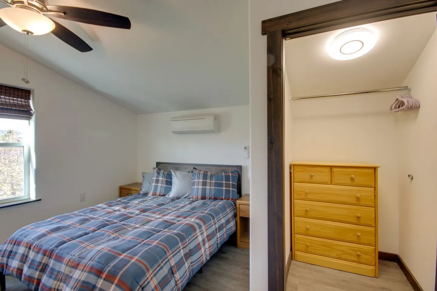 Bedroom with a bed made with blue plaid bedding, a ceiling fan, a window, and an adjacent walk-in closet with a wood dresser.