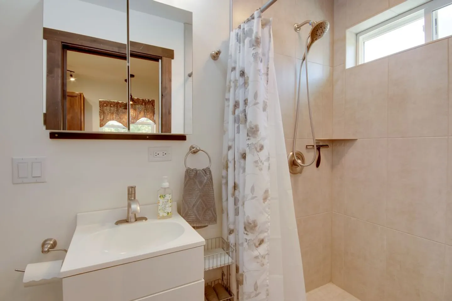 Bathroom with white vanity, medicine cabinet mirror, and tiled shower stall with curtain.