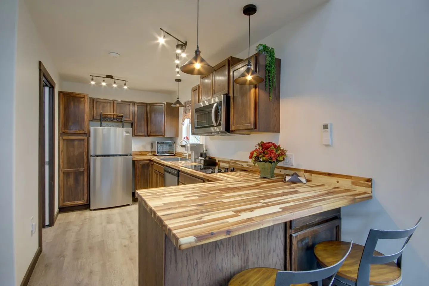 Kitchen with butcher-block peninsula, dark wood cabinets, stainless steel appliances, and pendant lighting.