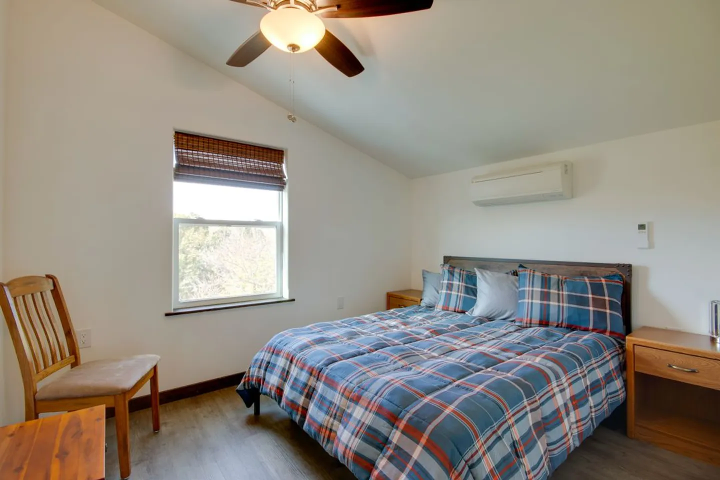 Bedroom with vaulted ceiling, a ceiling fan, a bed with a blue and red plaid comforter, a wooden chair, and nightstands.