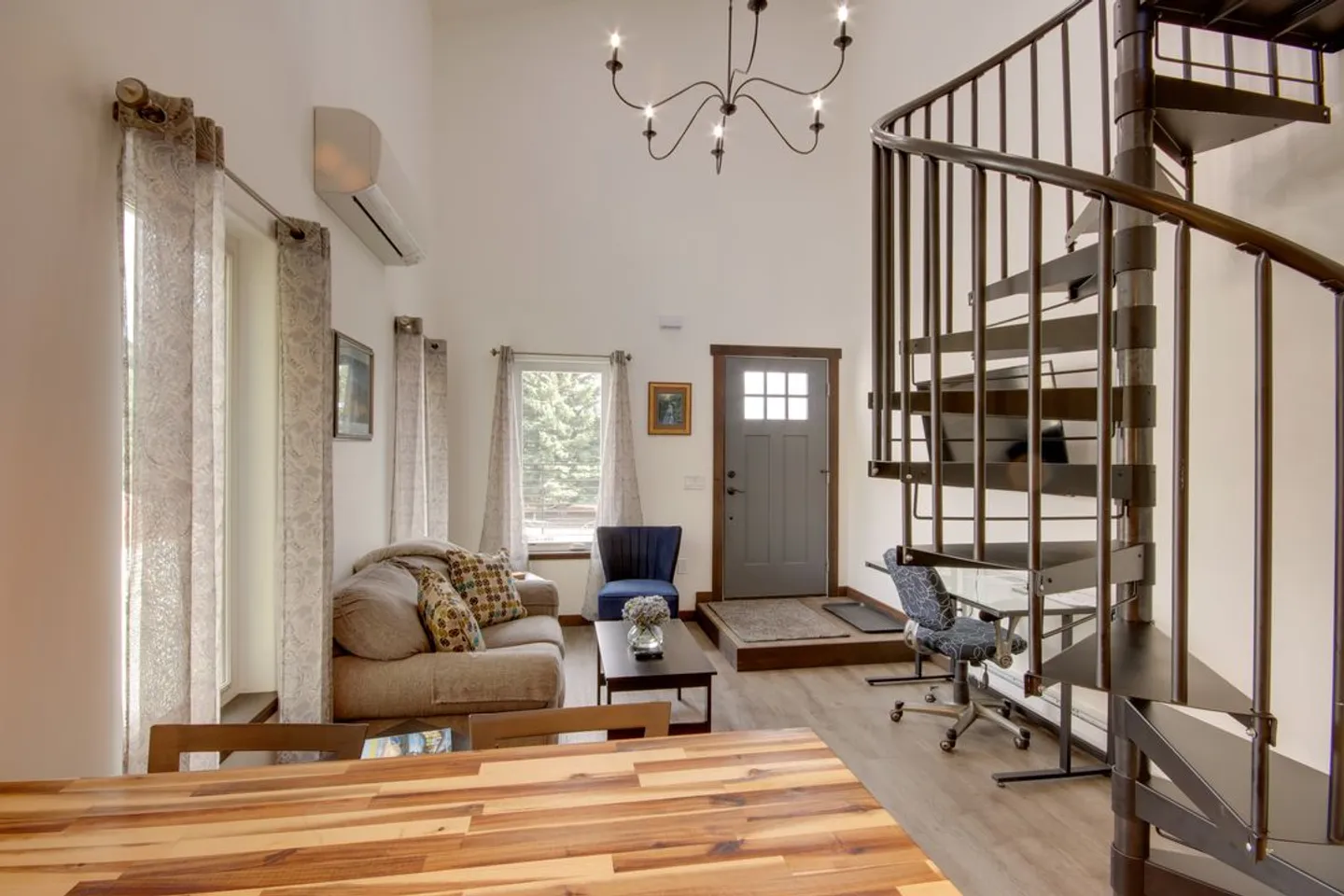 Living room with high ceilings, a spiral staircase, a sofa, and an entry door.
