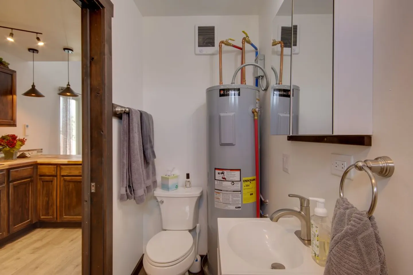 Bathroom with white toilet, sink vanity, mirrored cabinet, and an exposed water heater tank.