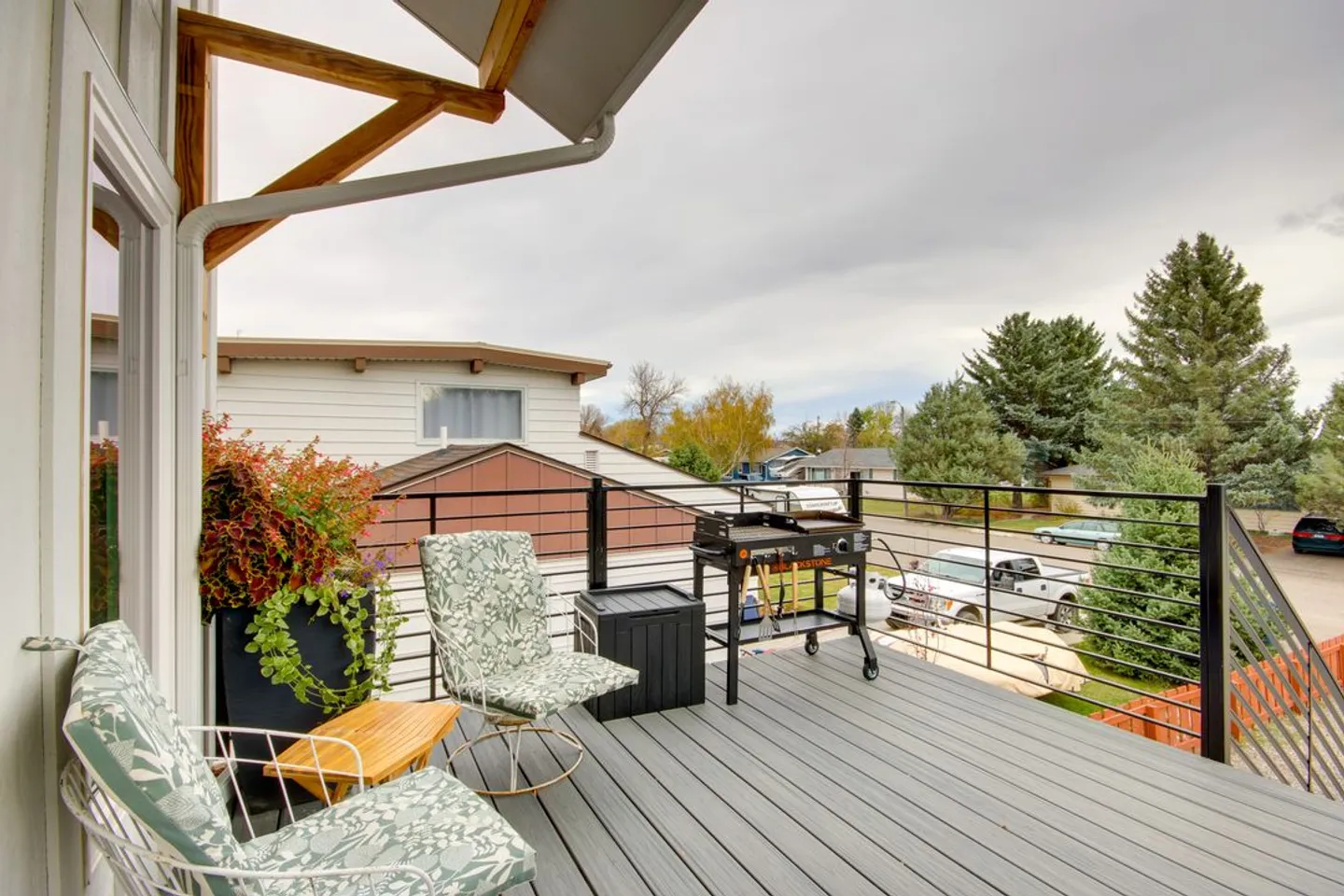 Elevated outdoor deck with gray composite decking, black railing, outdoor chairs, and a barbecue grill under an overcast sky.