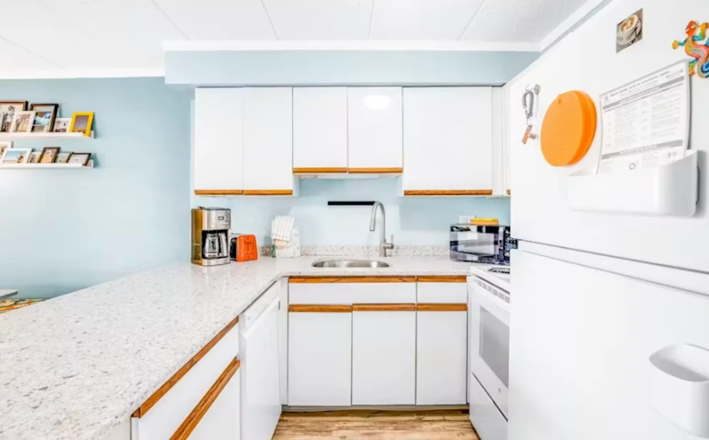 Compact kitchen featuring white cabinetry with wood trim, speckled countertops, a stainless steel sink, and white appliances.