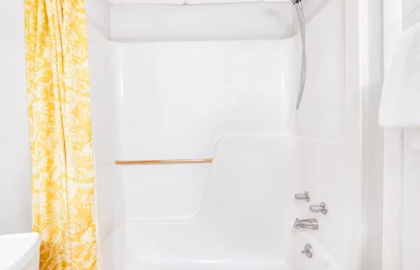 White shower and bathtub combination with a yellow patterned curtain and chrome fixtures.