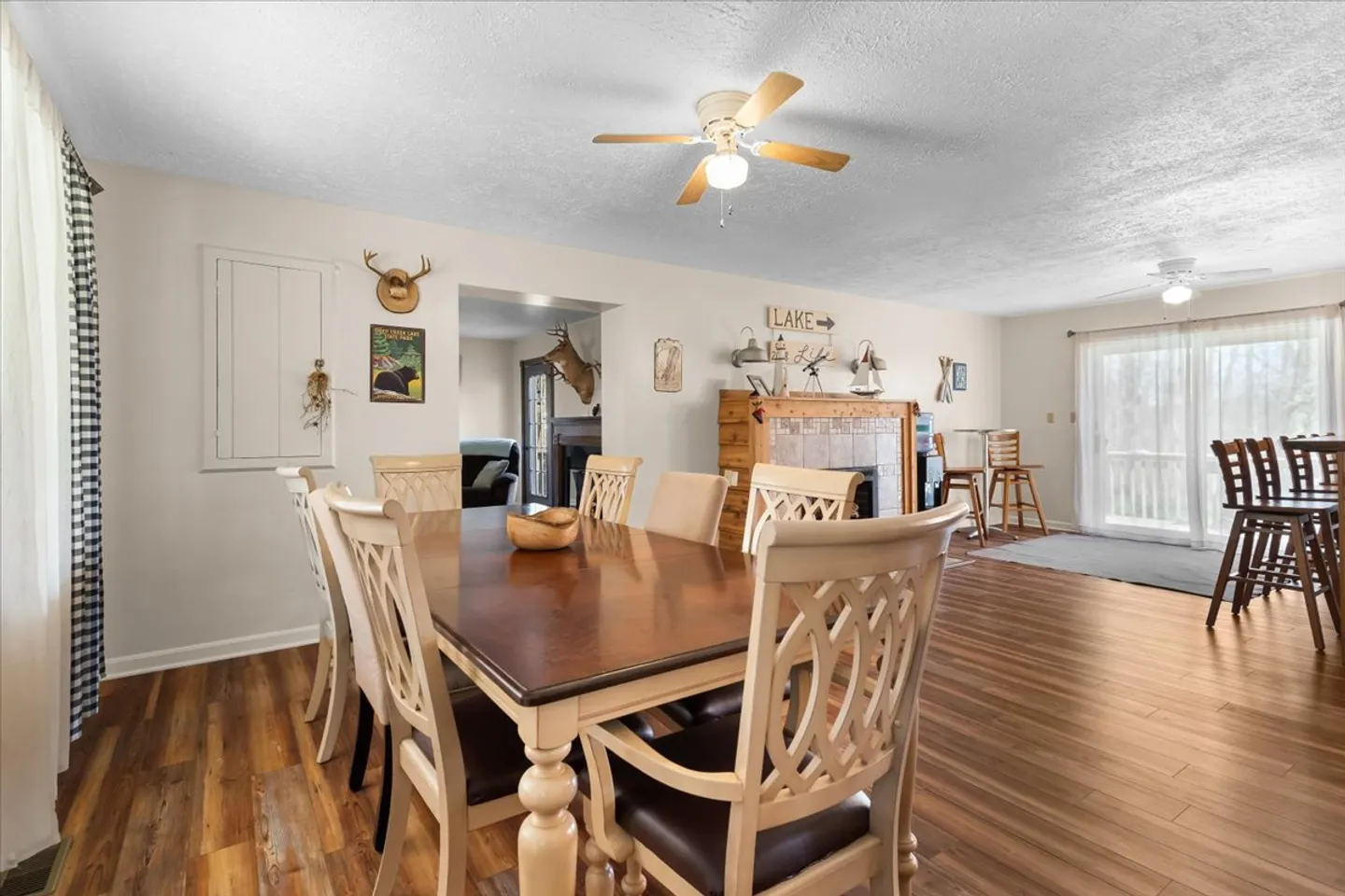 Dining room with a wooden dining table and chairs, wood-style flooring, a ceiling fan, and sliding glass doors in the background.