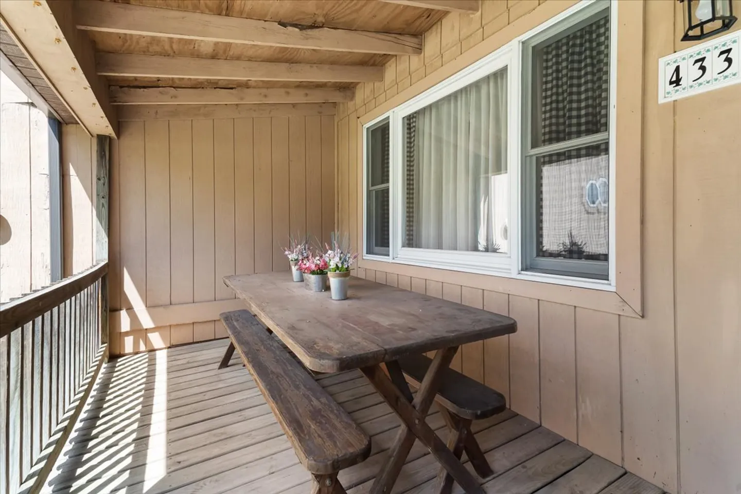 Covered wooden porch with a rustic picnic table and attached benches next to siding and a window.