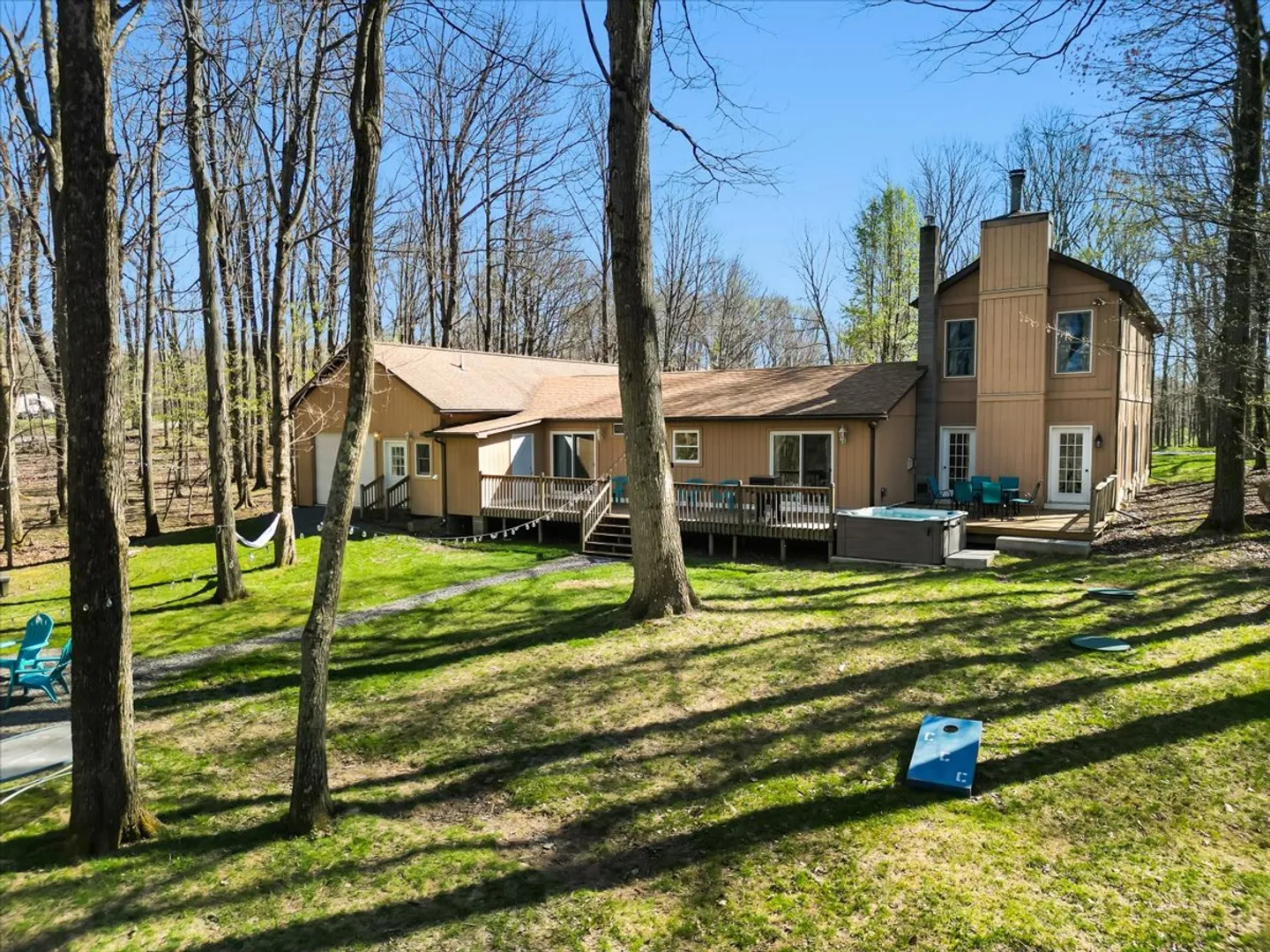 Rear exterior of a multi-level wood-sided home with a large deck, hot tub, and wooded yard.