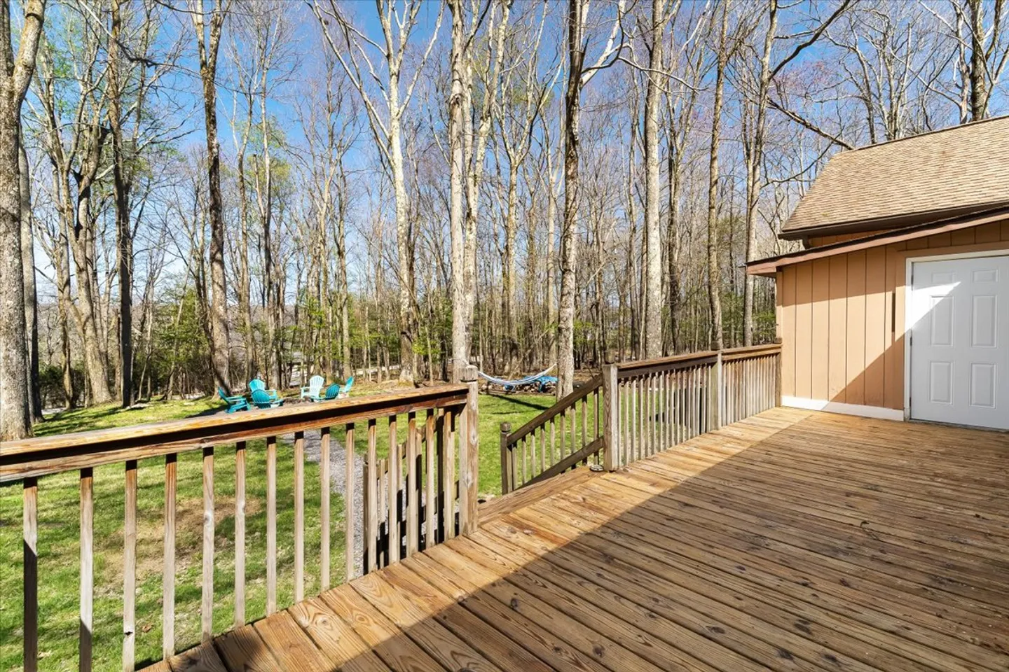 Elevated wooden deck with railing overlooking a wooded backyard with outdoor seating and a hammock.
