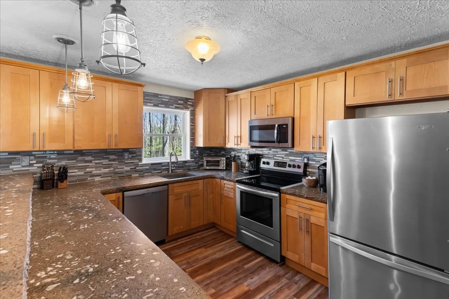 Kitchen with light wood cabinets, speckled brown countertops, stainless steel appliances, and a window above the sink.