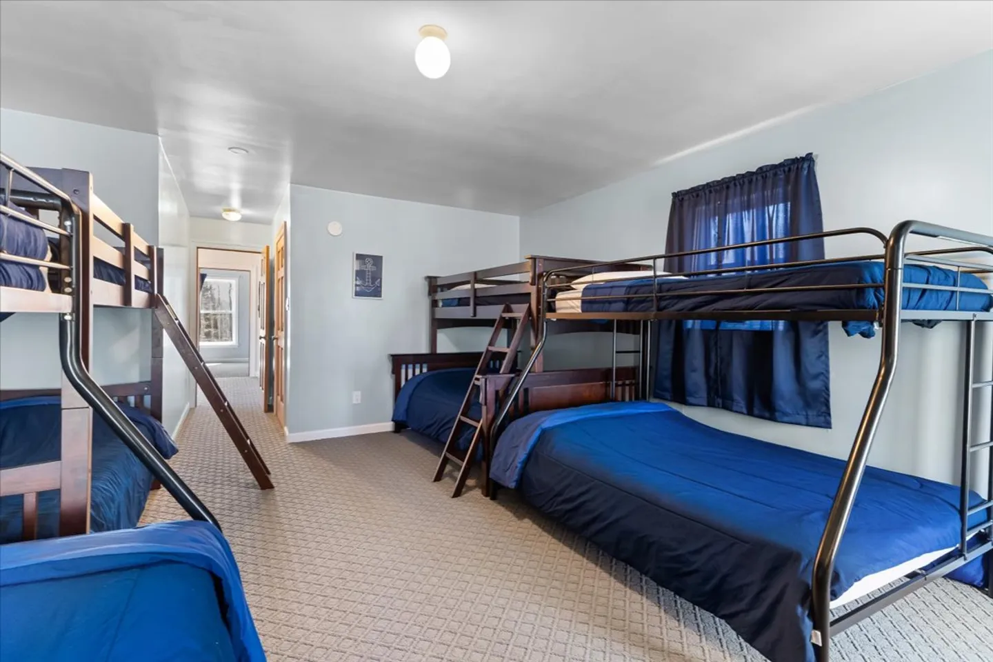 Bunk bedroom with patterned carpeting, light blue walls, and dark-toned bunk beds made with solid blue bedding.