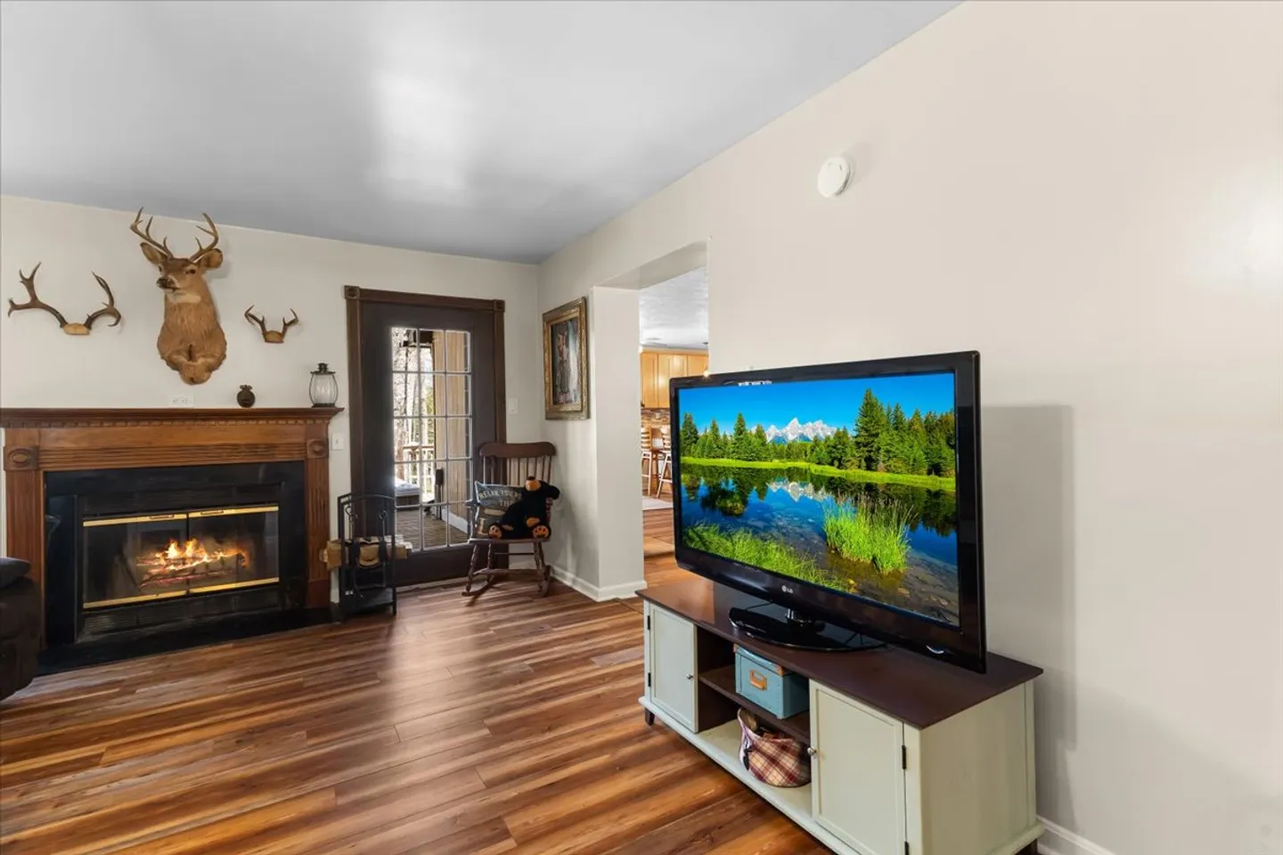 Living room with a fireplace, mounted television on a console, wooden flooring, and a glass-paneled exterior door.