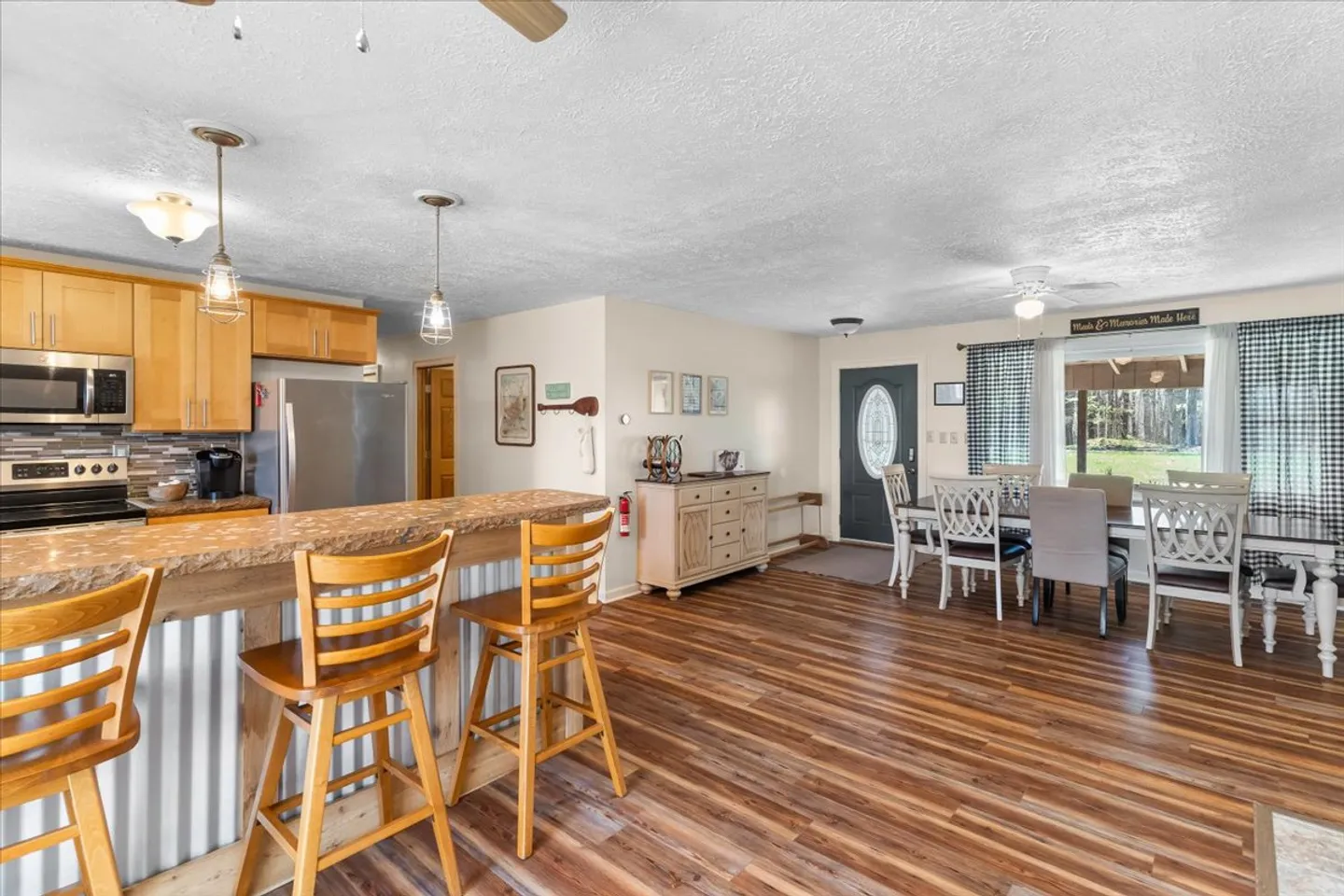 Open-concept kitchen and dining area featuring wood-look floors, a raised breakfast bar with wooden stools, and a dining table surrounded by chairs near a window.