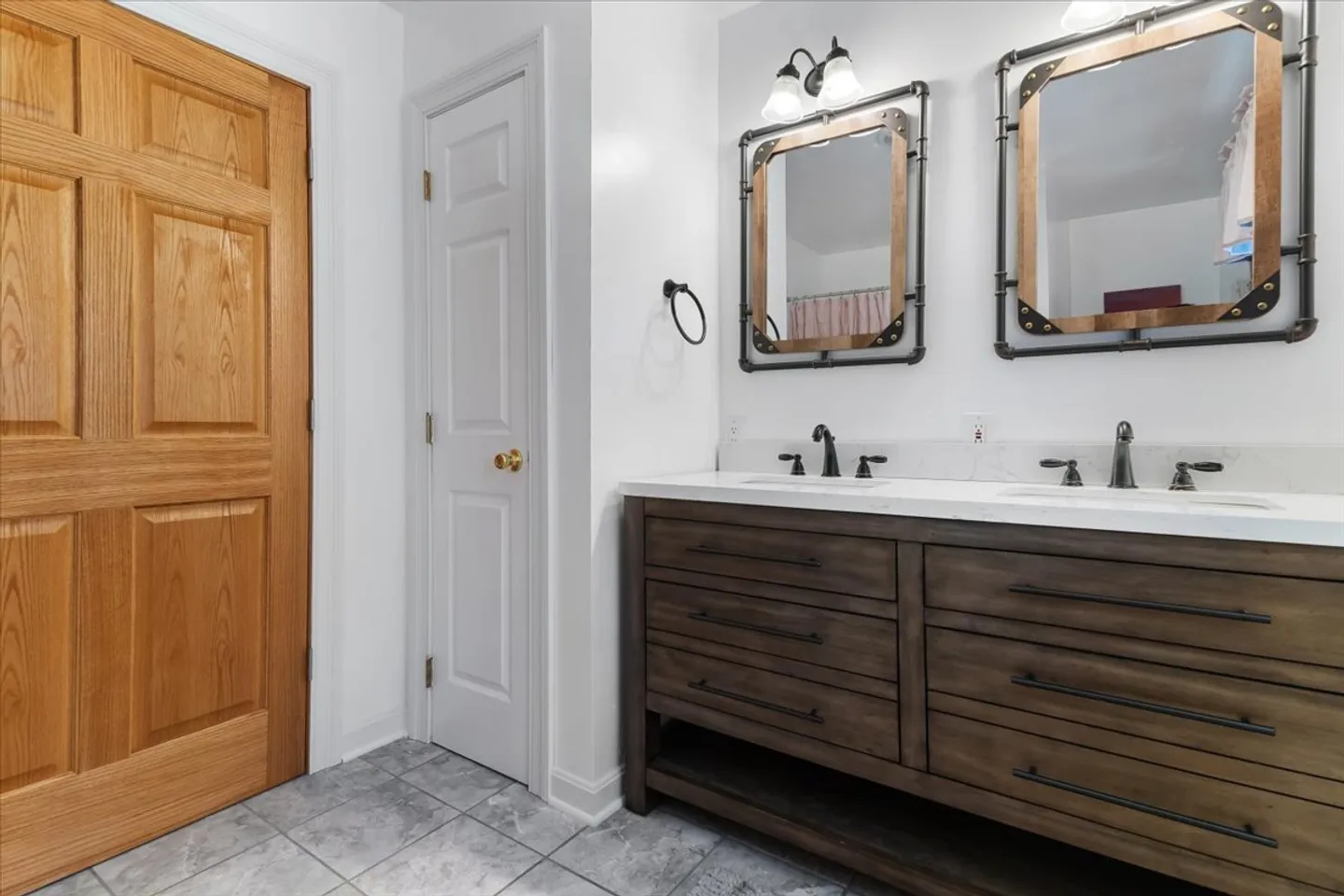 Bathroom with a double vanity featuring a dark wood base, white countertop, and two framed mirrors with industrial accents.