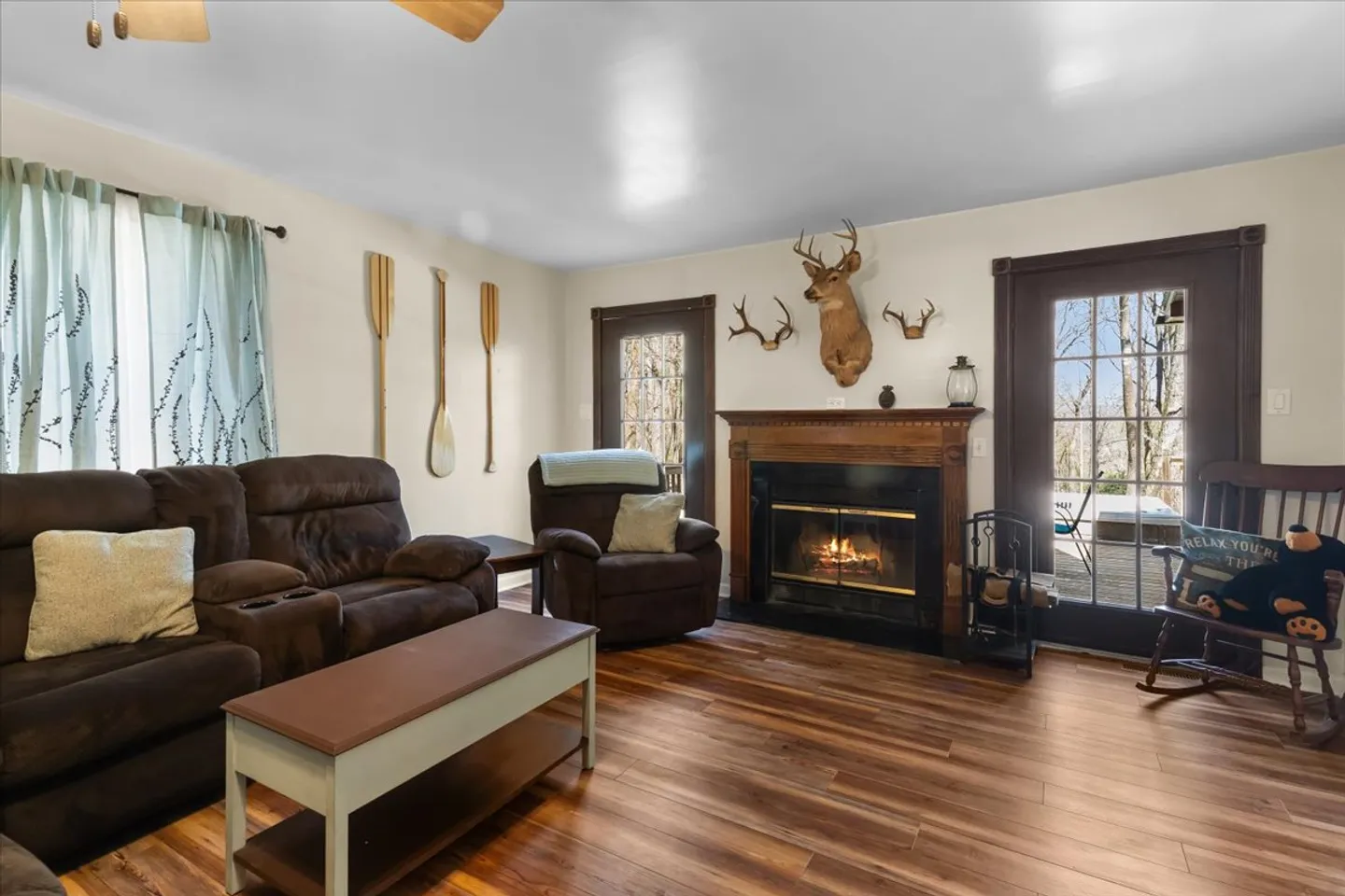 Living room with a lit fireplace, brown reclining sofa, armchair, rustic wall decor, and wood-look flooring.