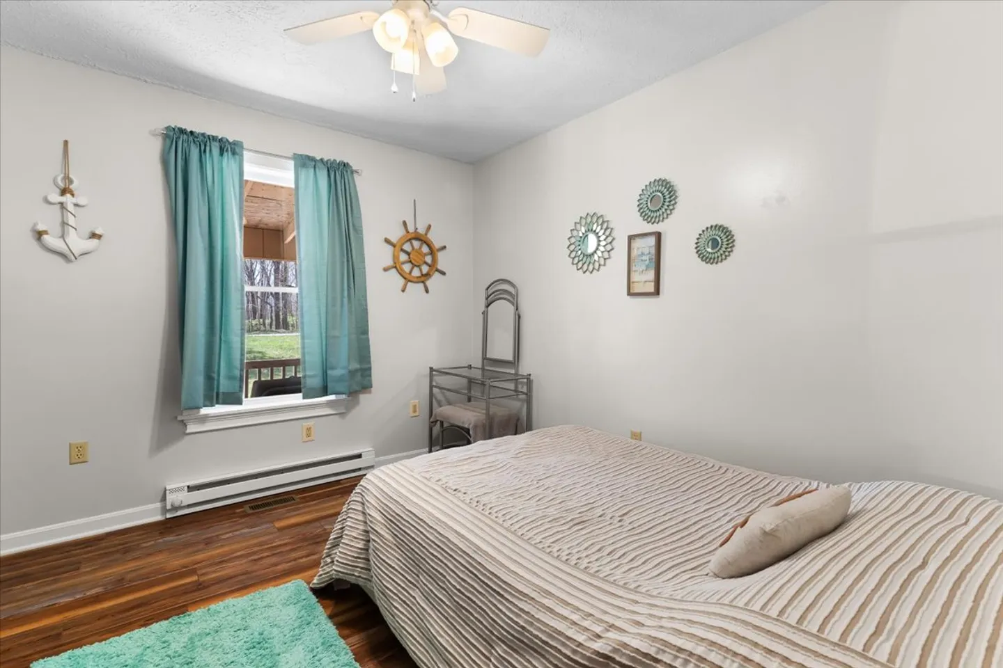 Bedroom with nautical wall decor, a bed with striped bedding, a window with teal curtains, and a vanity table.