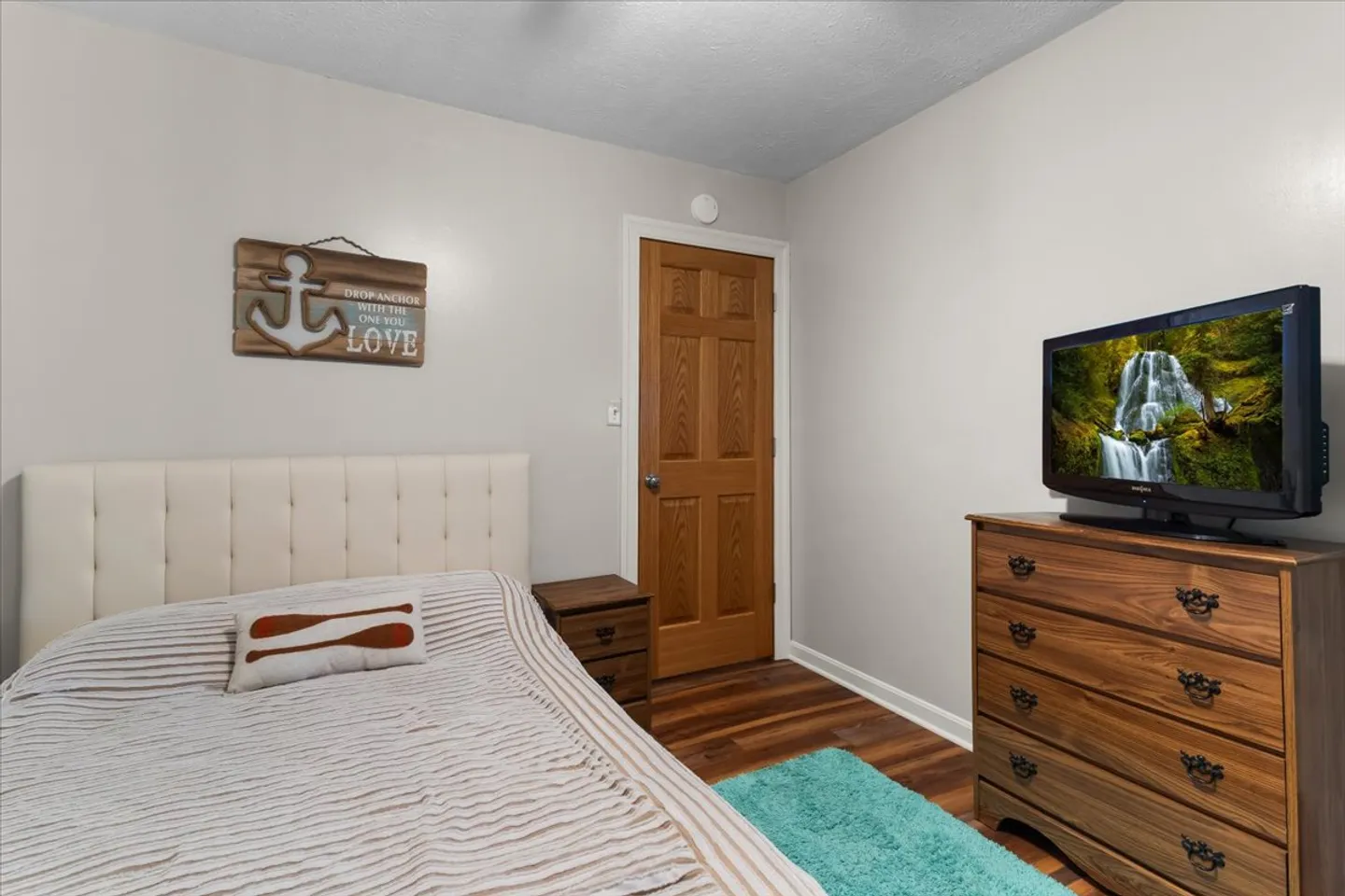 Bedroom with a tufted headboard, striped bedding, a wooden nightstand, and a dresser with a television.