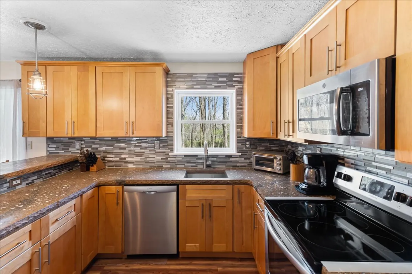 Kitchen interior featuring light wood cabinets, speckled dark countertops, stainless steel appliances, and a window above the sink.