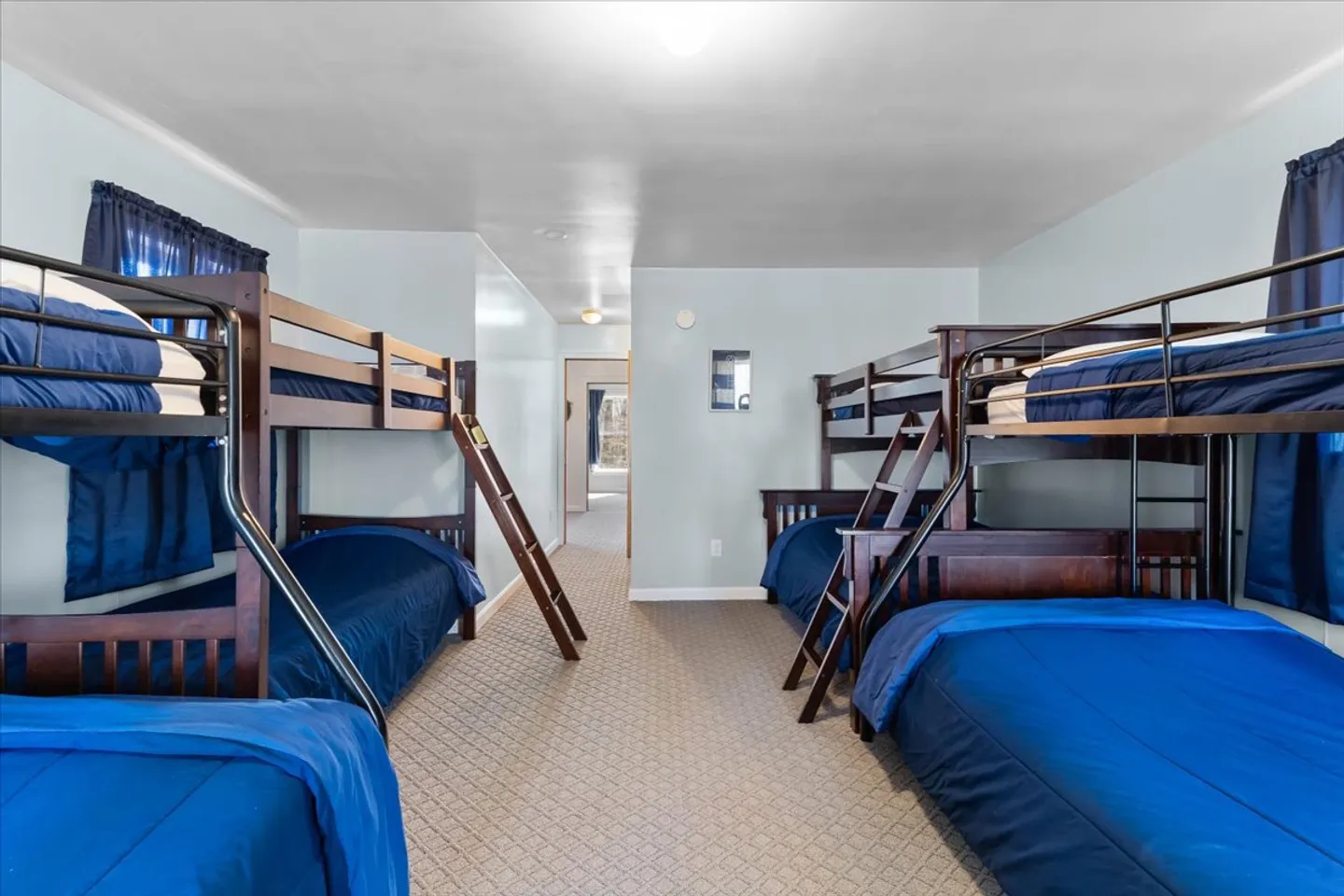 Bunk bedroom with multiple dark wood bunk beds dressed in bright blue bedding on patterned carpeting.