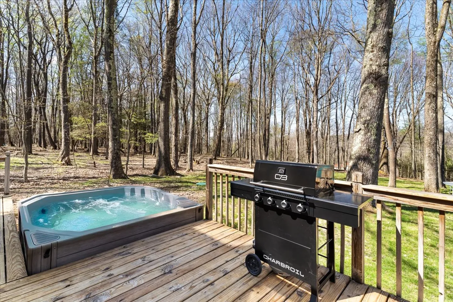 Outdoor wooden deck featuring a hot tub with bubbling water and a black Char-Broil grill, overlooking a wooded forest.