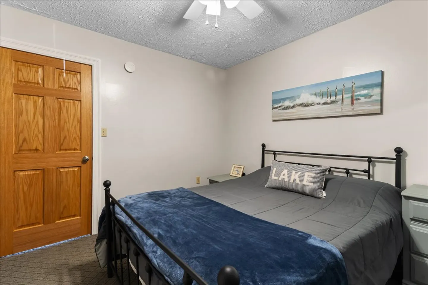Bedroom featuring a black metal bed frame with gray bedding, a ceiling fan, and a wood door.