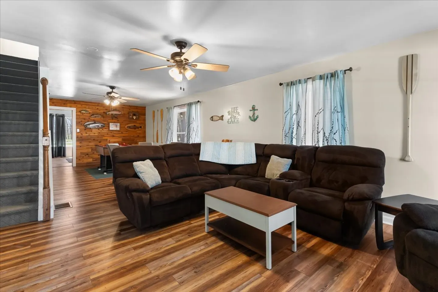 Living room featuring a large brown sectional sofa, a small coffee table, and wood-look flooring, with stairs on the left.