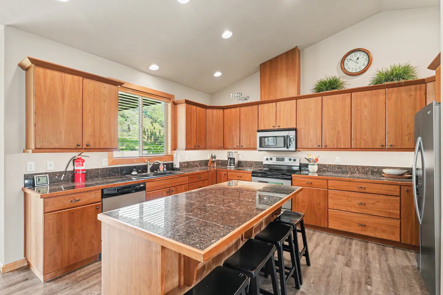 Kitchen with warm wood cabinetry, tiled countertops, a center island with barstools, and modern appliances.