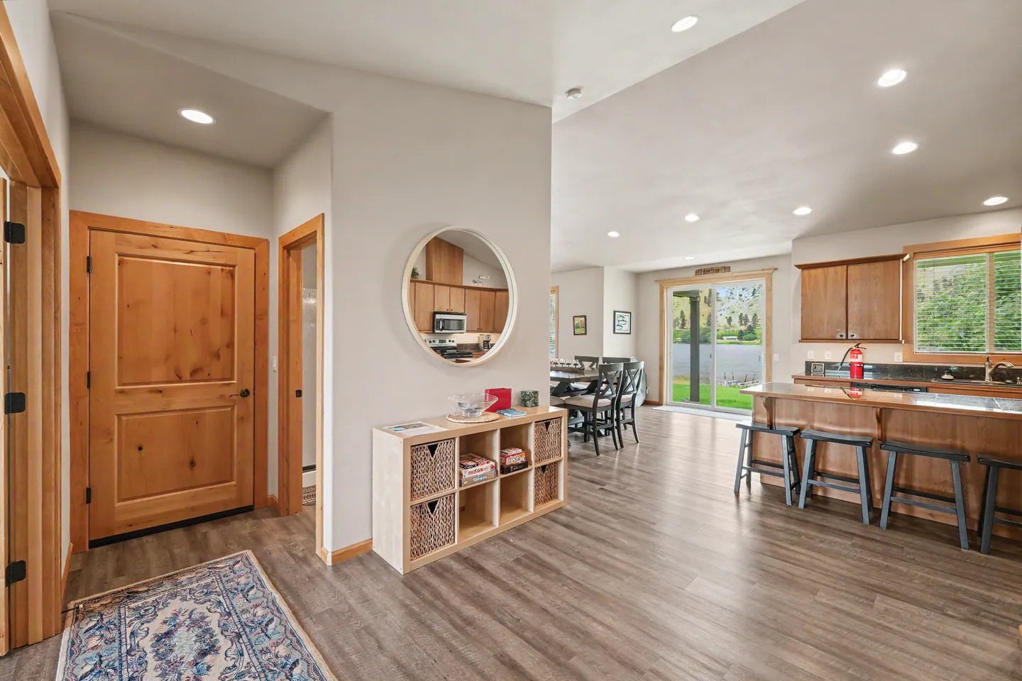 Entryway leading into an open-concept kitchen and dining area with wood-look flooring and a round wall mirror.