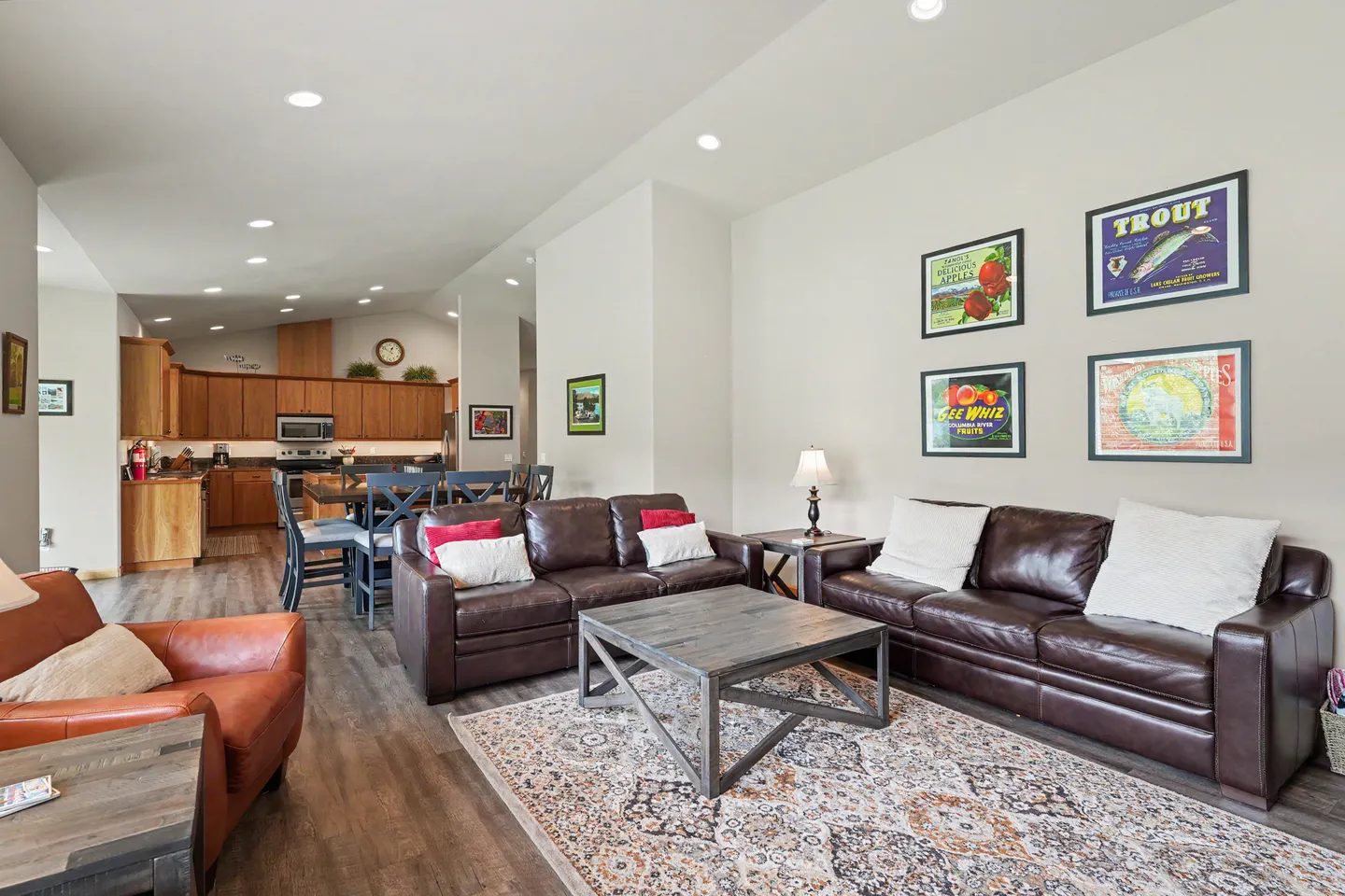 Open-concept living room with leather sofas, an patterned area rug, a coffee table, and views toward the dining table and kitchen.