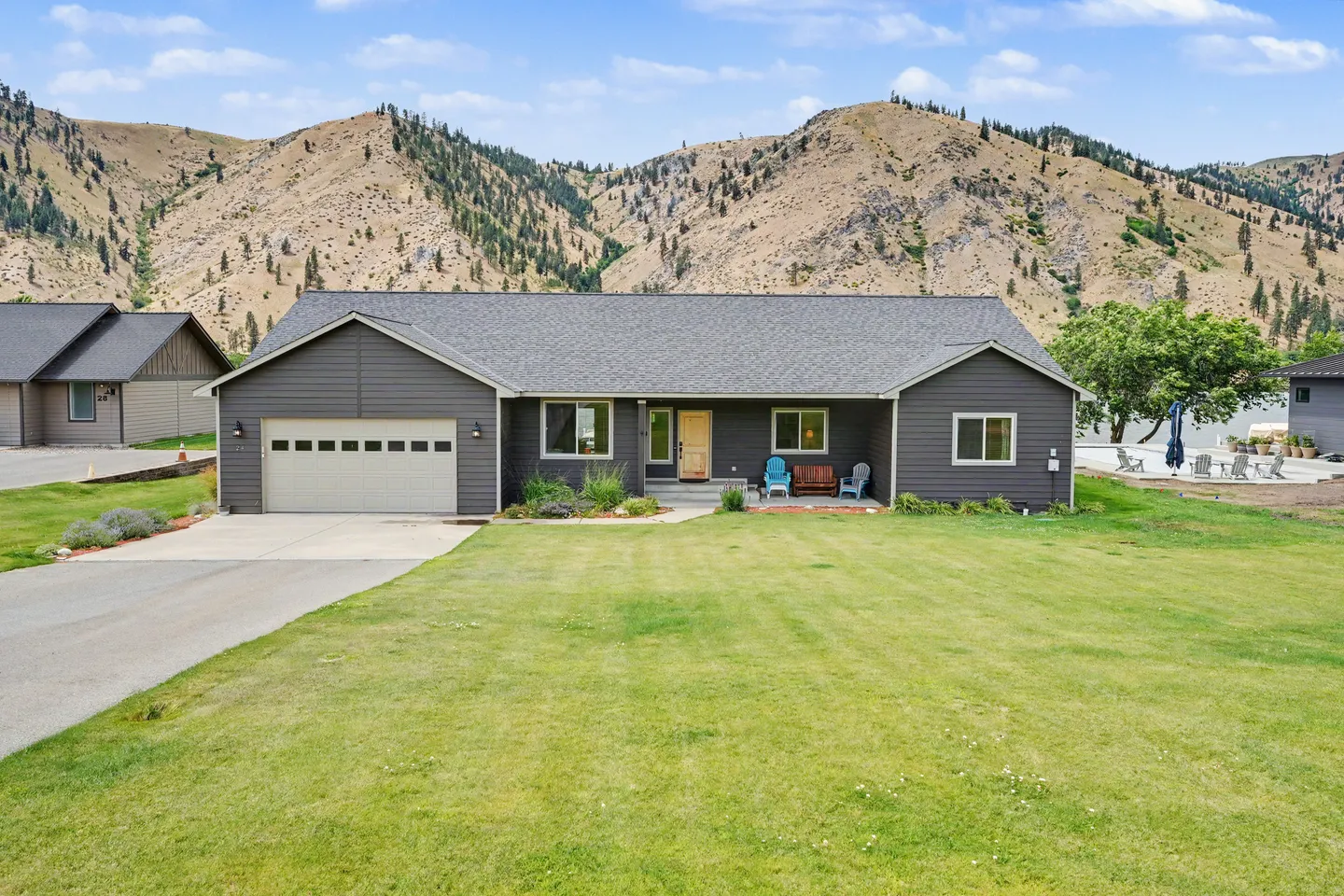 Front exterior of a single-story dark gray house with a two-car garage, front lawn, and mountainous hills in the background.