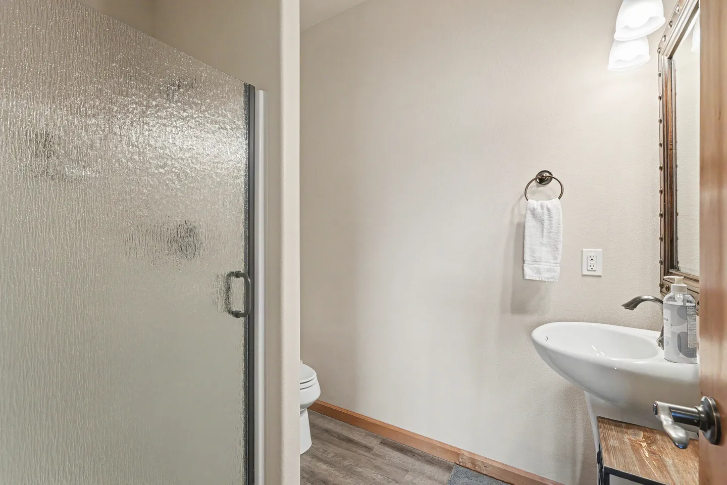 Bathroom with a textured glass shower door on the left, a pedestal-style sink on the right, and a toilet in the background.