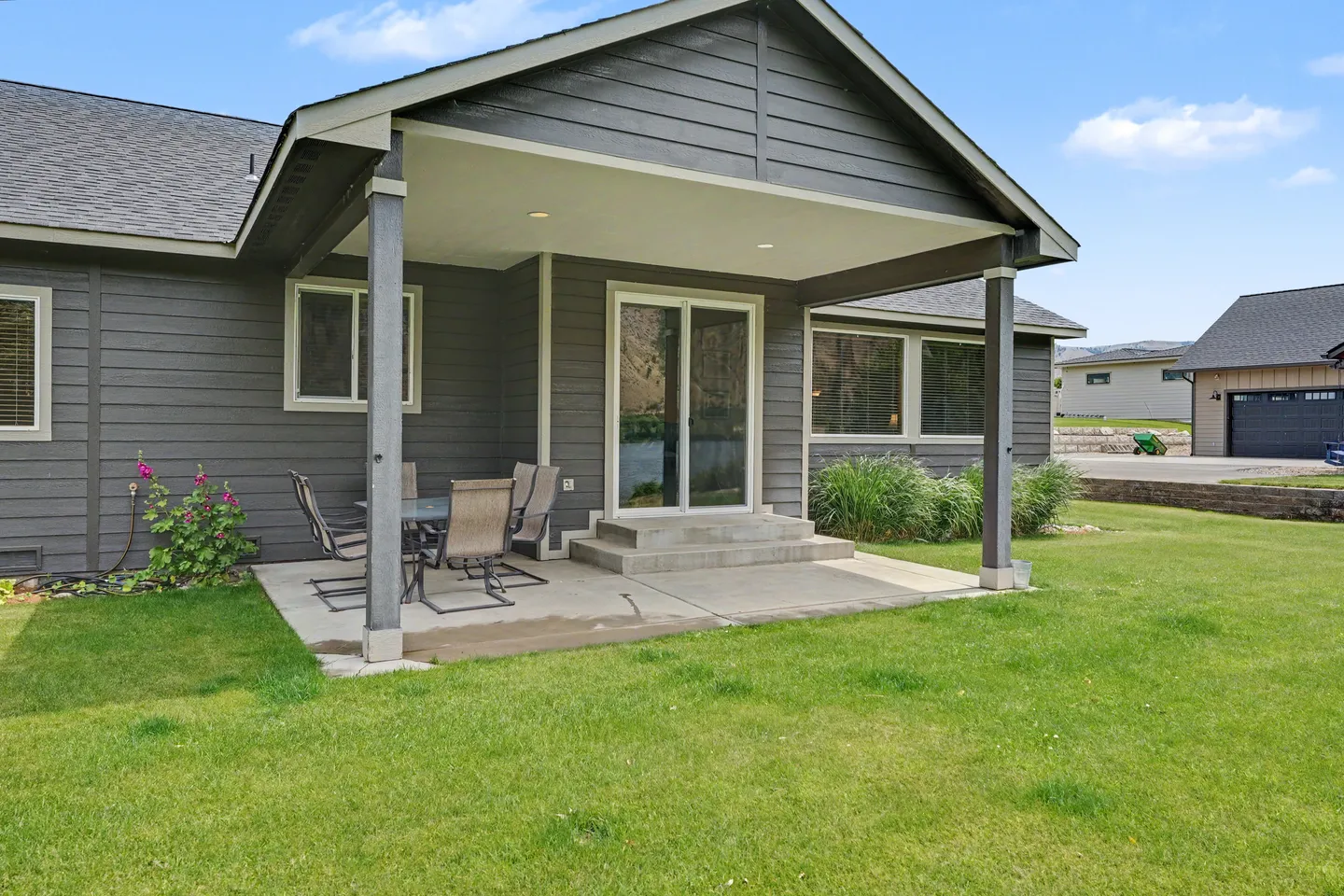 Exterior covered patio with concrete slab, outdoor dining table and chairs, sliding glass door, and green lawn.