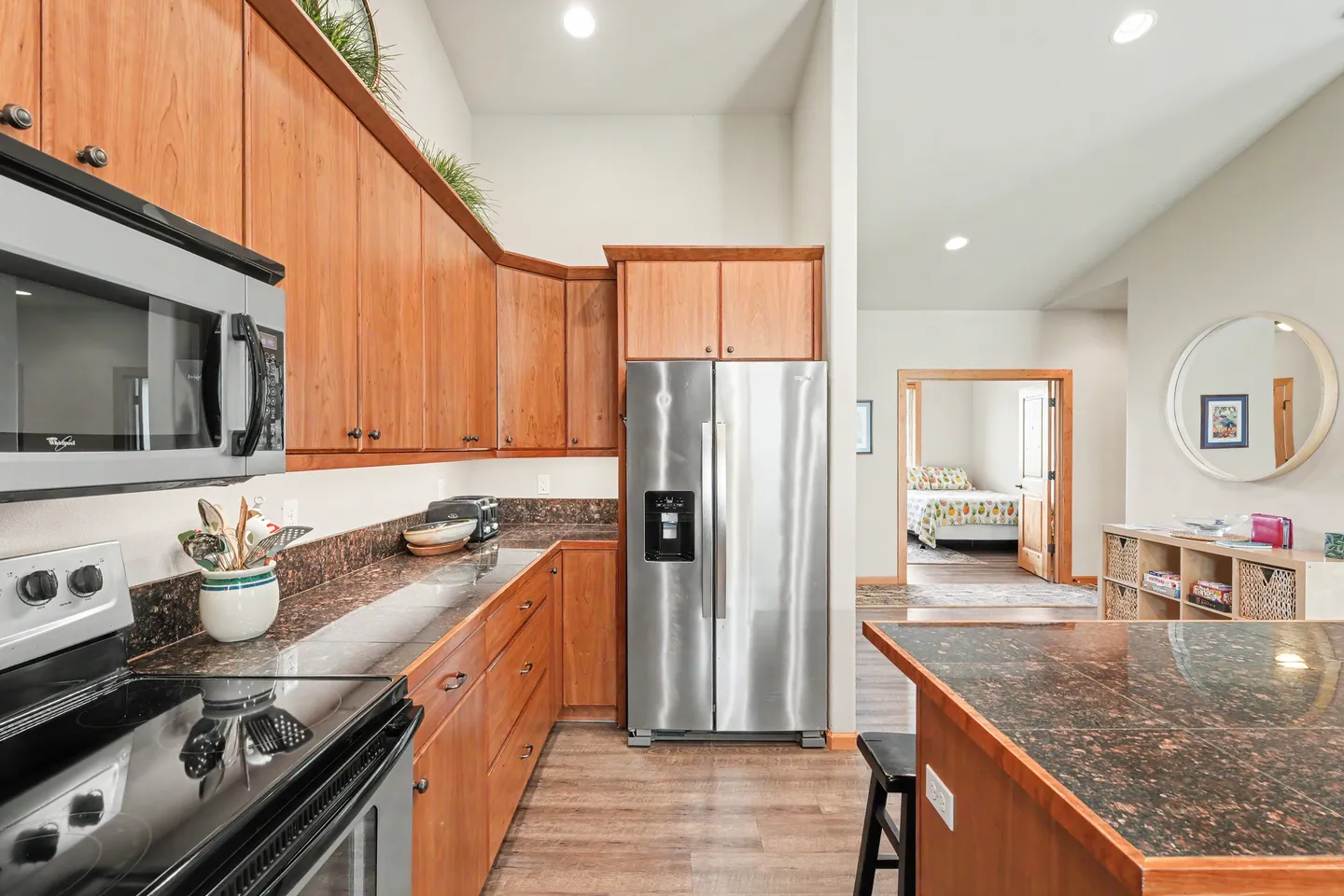 Kitchen with wooden cabinetry, speckled countertops, stainless steel appliances, and a view into an adjacent bedroom.
