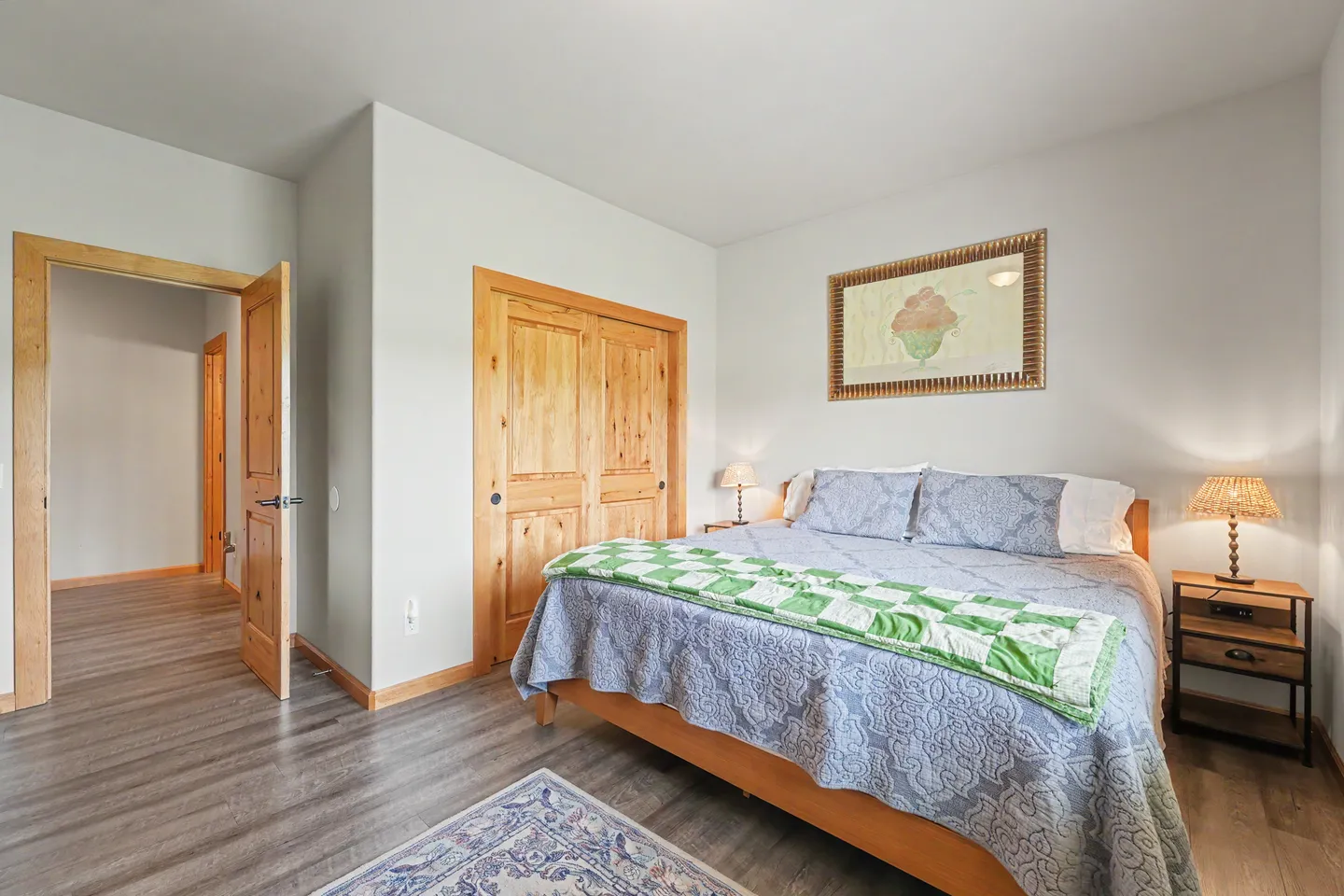 Bedroom featuring a wooden bed frame, patterned bedding, two nightstands with lamps, a closet with wooden doors, and an open doorway.