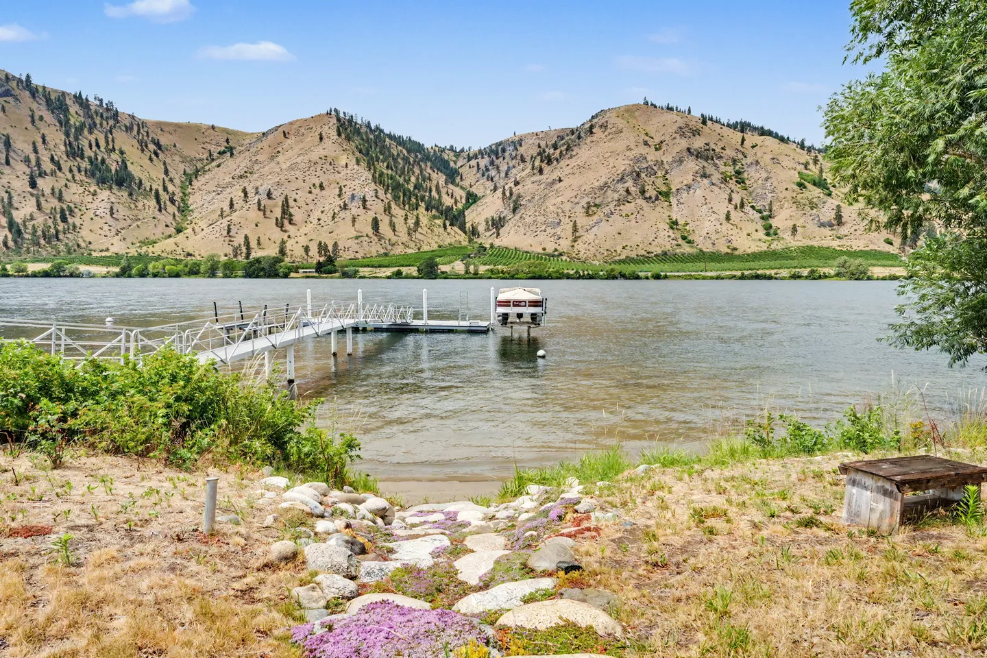 A long private boat dock extending into a wide lake or river with arid, rocky hills in the background.